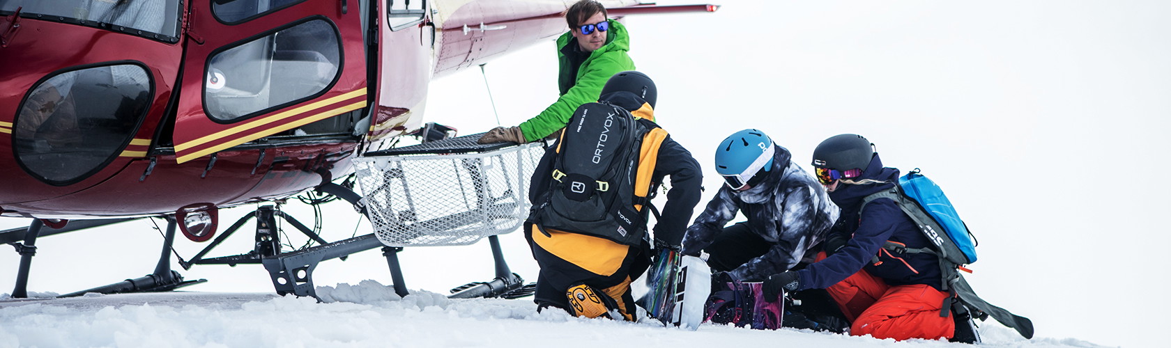 A group of skiers and snowboarders wearing backcountry backpacks in the snow