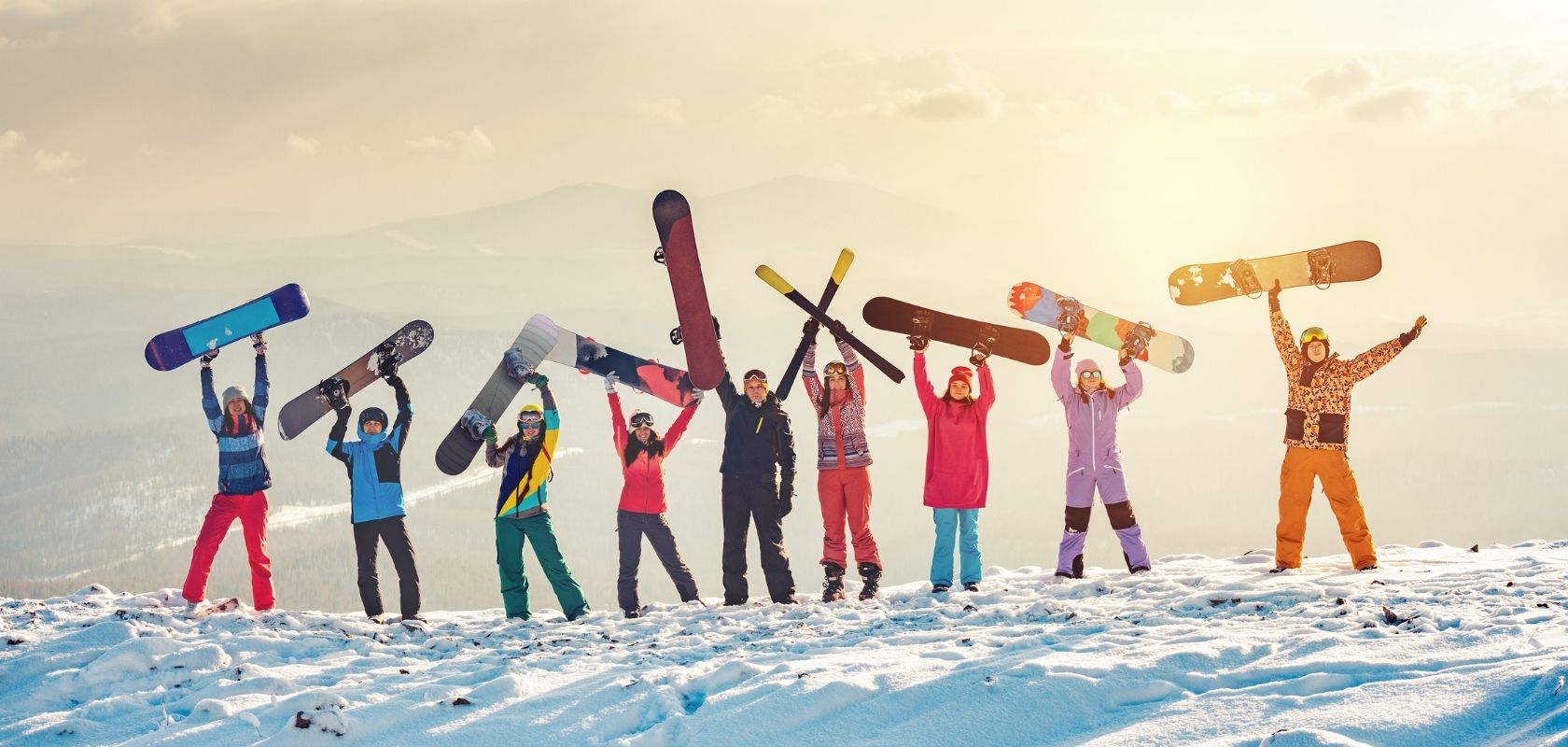 A group of snowboarders holding up brightly coloured snowboards 