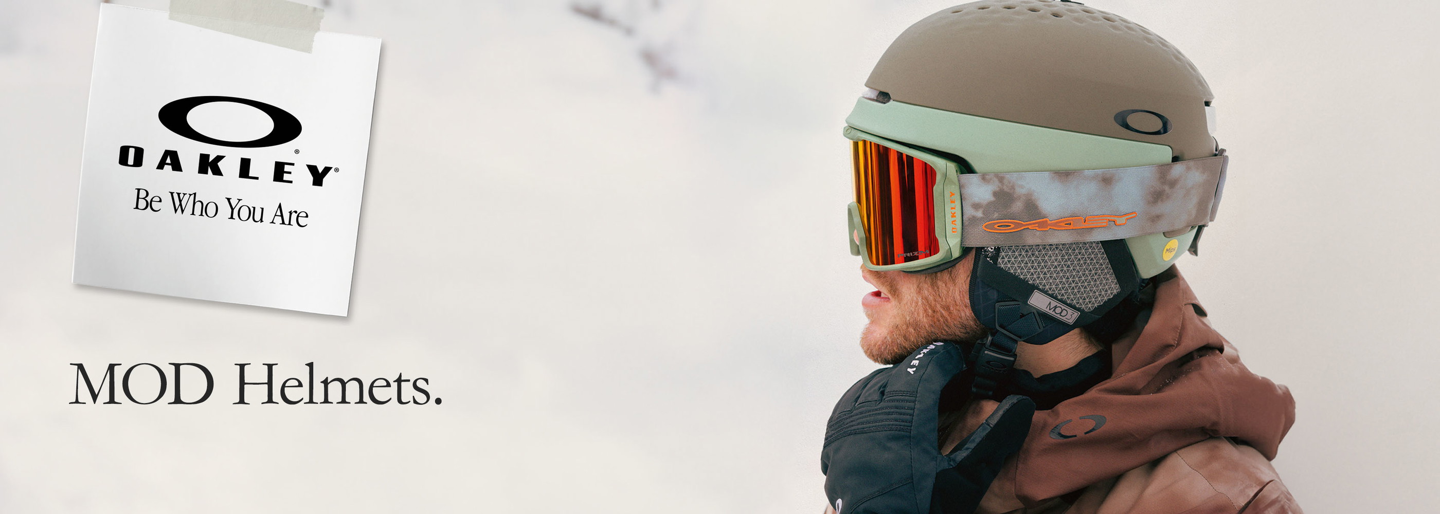A man in an orange coat holds up the Oakley Mod 5 and Mod 1 helmets