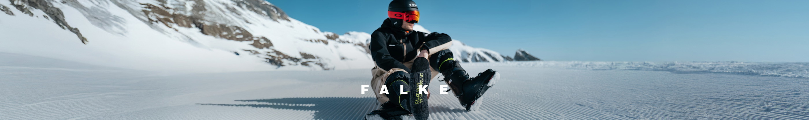 Shop Falke collection. A skiier resting on the snowwith his boots off